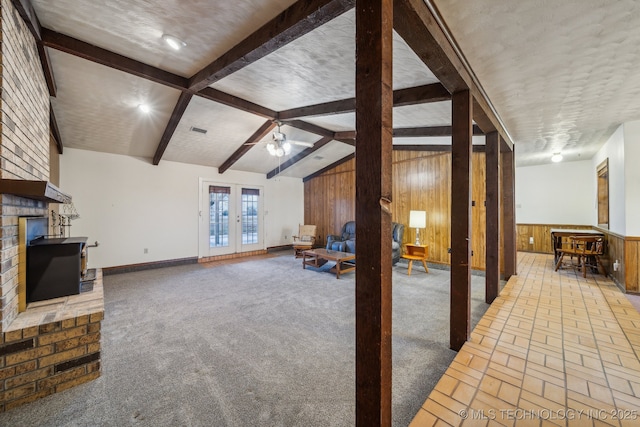 living room with wooden walls, lofted ceiling with beams, ceiling fan, a brick fireplace, and french doors