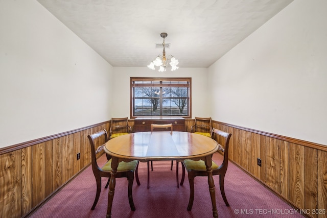 dining area with a chandelier, light colored carpet, and wooden walls