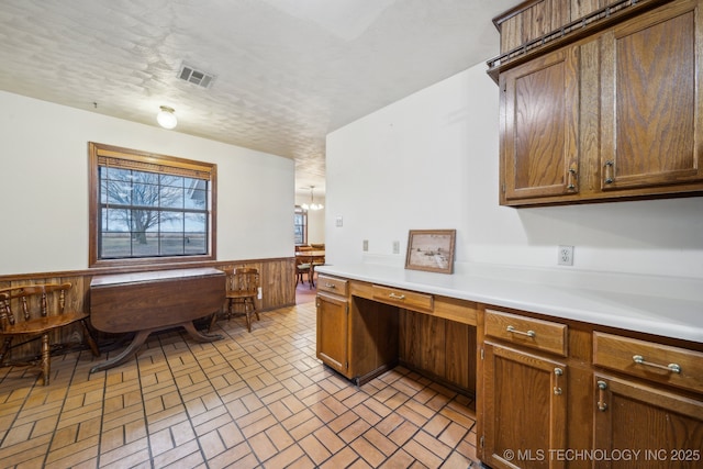 kitchen featuring an inviting chandelier, built in desk, a textured ceiling, and wood walls