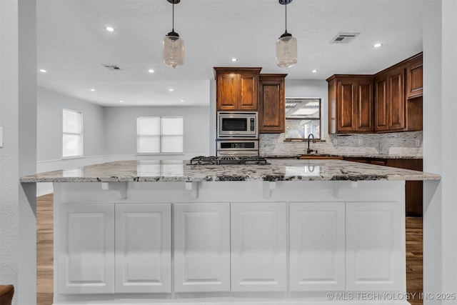 kitchen with pendant lighting, appliances with stainless steel finishes, light stone counters, tasteful backsplash, and light wood-type flooring