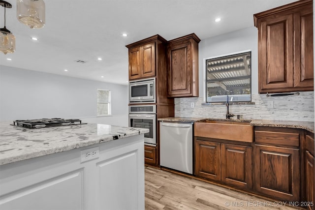 kitchen featuring sink, stainless steel appliances, light stone countertops, decorative backsplash, and light wood-type flooring