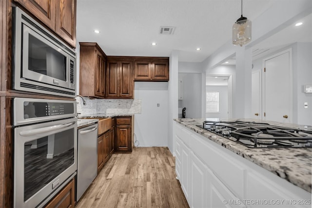 kitchen featuring tasteful backsplash, white cabinets, light stone counters, stainless steel appliances, and light wood-type flooring