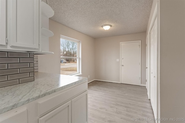 kitchen with light stone counters, a textured ceiling, white cabinets, and light wood-type flooring