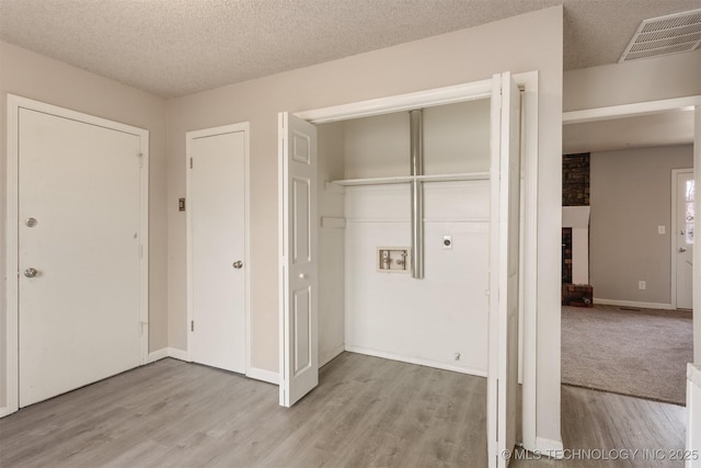 washroom with a brick fireplace, light hardwood / wood-style floors, hookup for a washing machine, and a textured ceiling