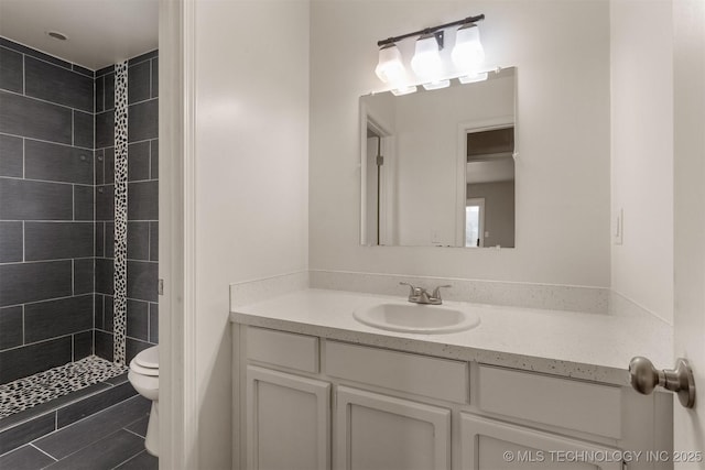 bathroom with vanity, tiled shower, and toilet