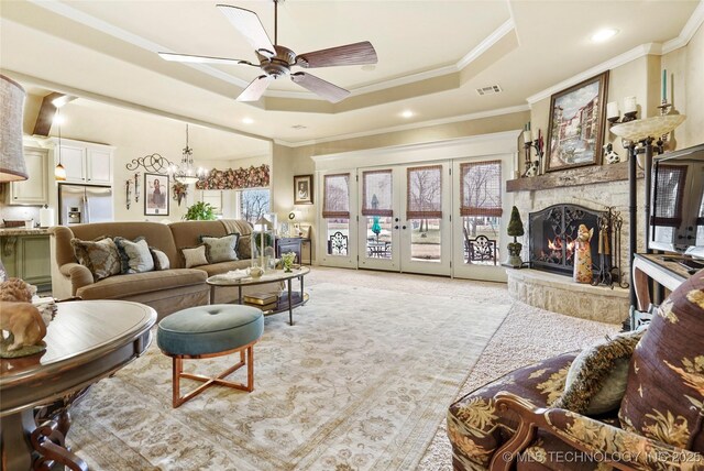 carpeted living room featuring a raised ceiling, crown molding, ceiling fan with notable chandelier, and a fireplace