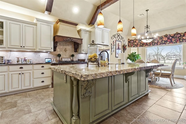 kitchen with hanging light fixtures, a center island with sink, dark stone counters, and premium range hood