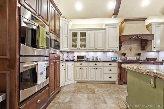 kitchen featuring decorative backsplash, custom exhaust hood, dark stone counters, and appliances with stainless steel finishes