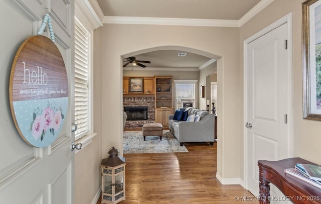 foyer featuring hardwood / wood-style flooring, ceiling fan, ornamental molding, and a brick fireplace