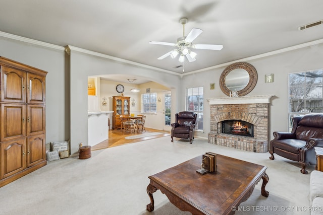 living room featuring ceiling fan, ornamental molding, light carpet, and a fireplace