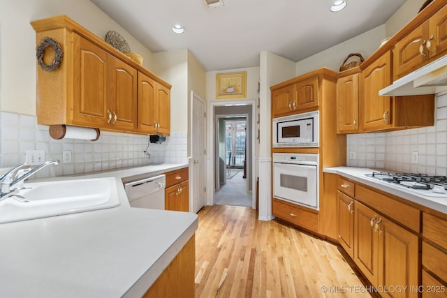 kitchen with white appliances, sink, decorative backsplash, and light wood-type flooring