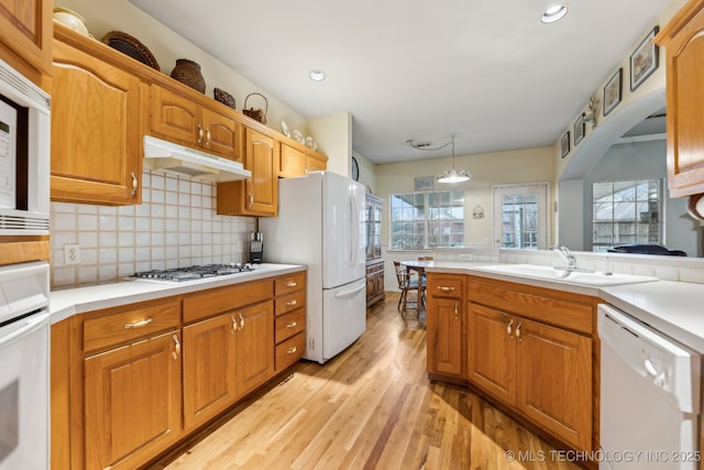 kitchen with sink, tasteful backsplash, decorative light fixtures, light hardwood / wood-style flooring, and white appliances