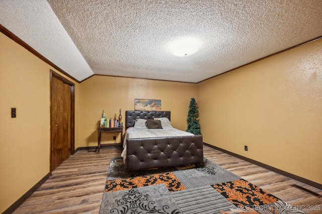 bedroom featuring crown molding, wood-type flooring, a textured ceiling, and vaulted ceiling