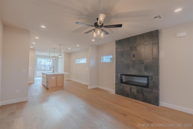 unfurnished living room featuring a fireplace, light hardwood / wood-style flooring, sink, and ceiling fan