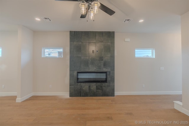 unfurnished living room with ceiling fan, a tiled fireplace, and light hardwood / wood-style flooring