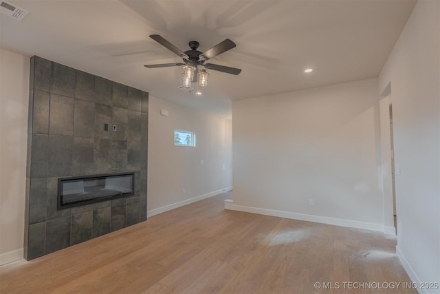 unfurnished living room featuring ceiling fan, a tiled fireplace, and light wood-type flooring