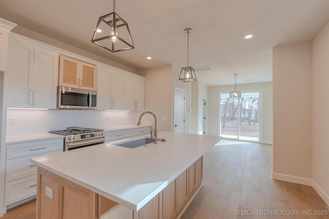 kitchen featuring appliances with stainless steel finishes, a kitchen island with sink, white cabinets, and decorative light fixtures