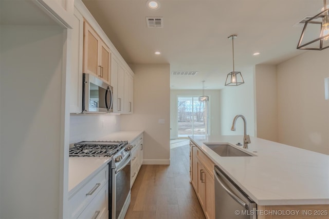 kitchen featuring sink, decorative light fixtures, appliances with stainless steel finishes, a kitchen island with sink, and white cabinets