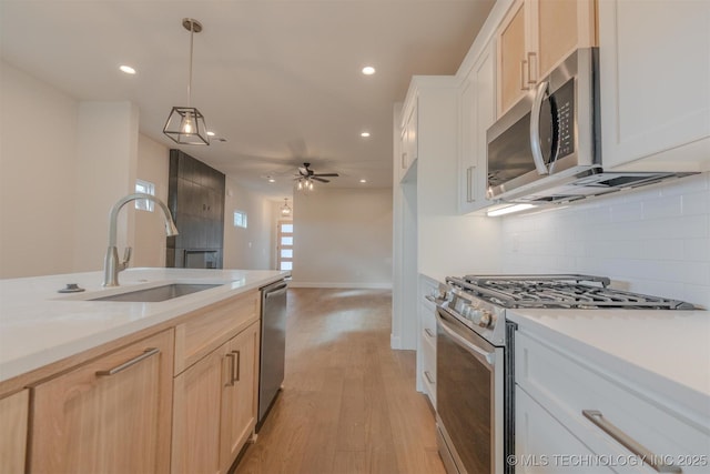 kitchen with light brown cabinetry, sink, tasteful backsplash, hanging light fixtures, and stainless steel appliances