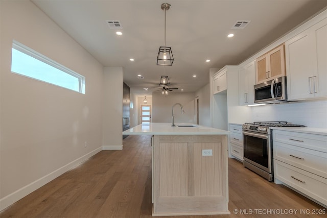 kitchen featuring sink, white cabinets, hanging light fixtures, stainless steel appliances, and a center island with sink