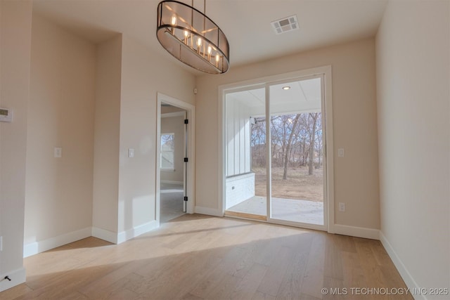 empty room with an inviting chandelier and light hardwood / wood-style flooring