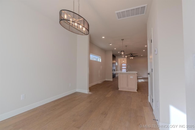 interior space featuring sink, decorative light fixtures, light hardwood / wood-style flooring, an island with sink, and ceiling fan with notable chandelier