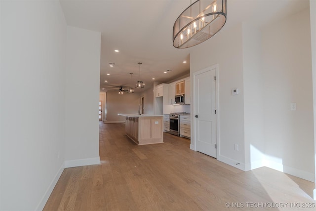 kitchen with light hardwood / wood-style flooring, a kitchen island with sink, pendant lighting, stainless steel appliances, and ceiling fan with notable chandelier