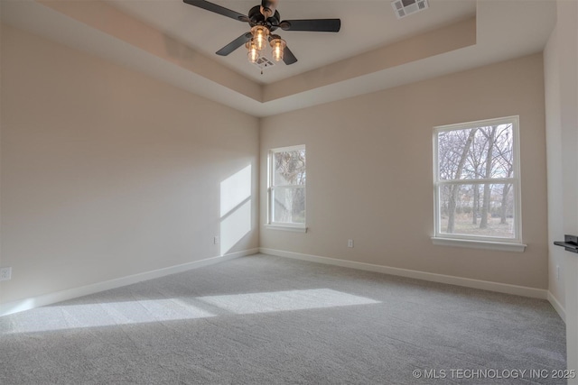 spare room with a tray ceiling, light colored carpet, and ceiling fan