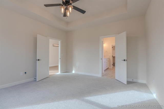 unfurnished bedroom with ceiling fan, light colored carpet, ensuite bath, and a tray ceiling