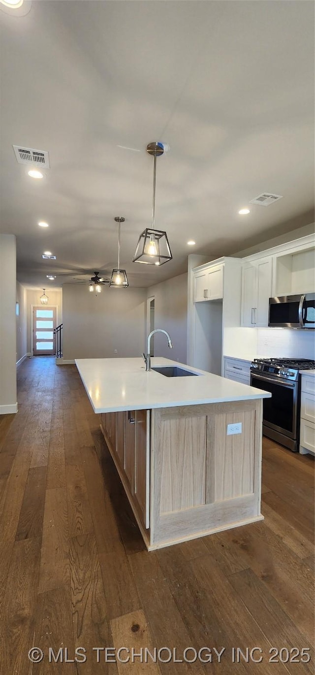 kitchen with appliances with stainless steel finishes, a sink, dark wood finished floors, a center island with sink, and recessed lighting