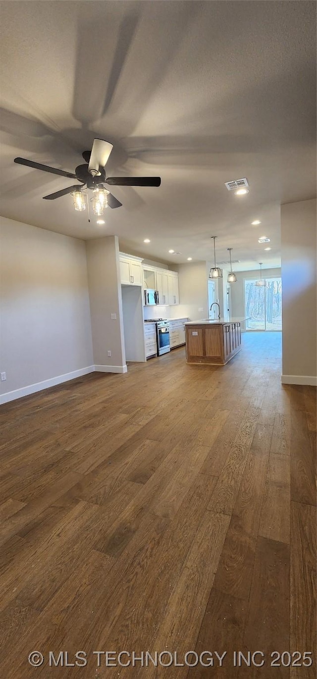 unfurnished living room featuring visible vents, baseboards, dark wood-style floors, a ceiling fan, and a sink