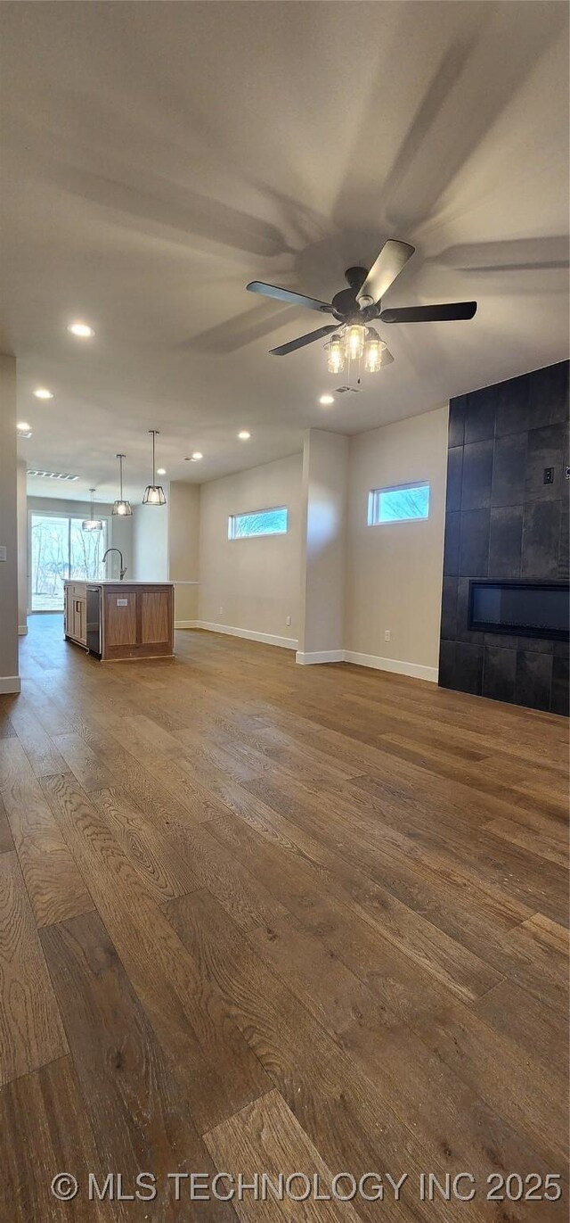 unfurnished living room featuring wood finished floors, a tile fireplace, baseboards, and recessed lighting