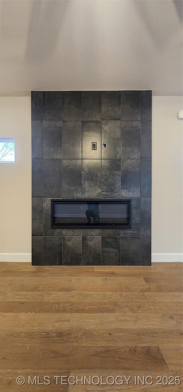 detailed view of a fireplace, wood finished floors, and baseboards