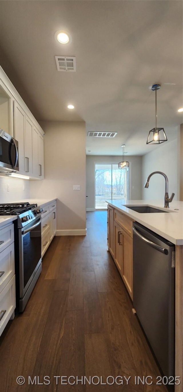 kitchen featuring visible vents, dark wood-style flooring, a sink, stainless steel appliances, and light countertops