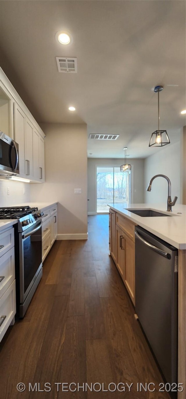 kitchen with appliances with stainless steel finishes, a sink, dark wood-style floors, light countertops, and baseboards