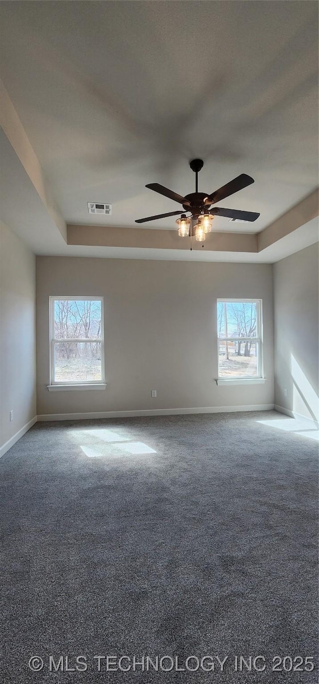 carpeted spare room with baseboards, healthy amount of natural light, ceiling fan, and a raised ceiling