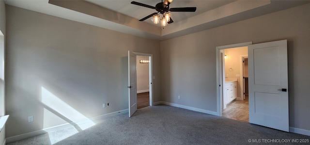 unfurnished bedroom featuring light carpet, baseboards, ceiling fan, and a tray ceiling