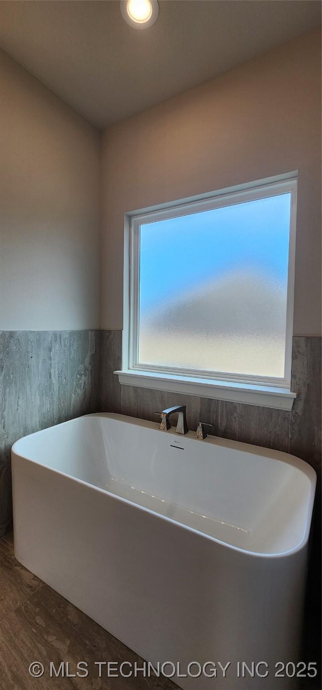 bathroom with a freestanding bath, wood finished floors, and wainscoting