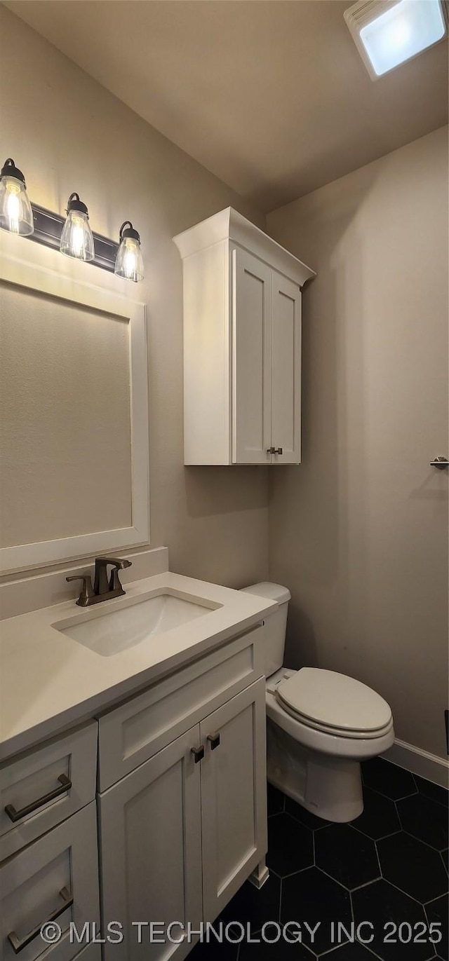 half bath featuring tile patterned floors, baseboards, toilet, and vanity