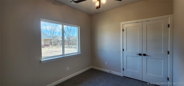 unfurnished bedroom featuring dark colored carpet, a closet, baseboards, and a ceiling fan