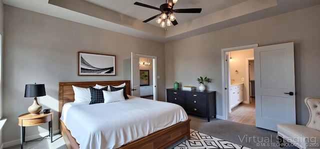 bedroom with light carpet, baseboards, a tray ceiling, ensuite bathroom, and a ceiling fan