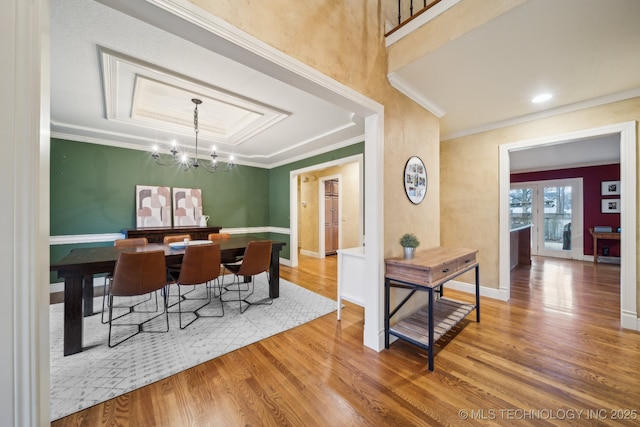 dining room featuring a tray ceiling, hardwood / wood-style floors, a notable chandelier, and ornamental molding