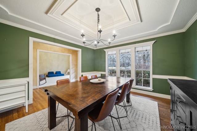 dining area with hardwood / wood-style flooring, ornamental molding, a chandelier, and a tray ceiling