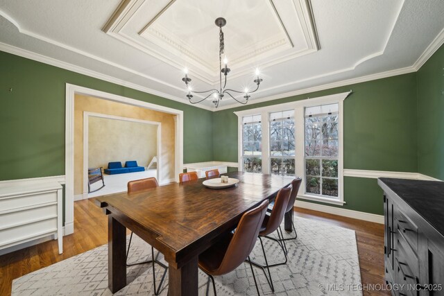 dining room featuring hardwood / wood-style floors, crown molding, a raised ceiling, and a chandelier