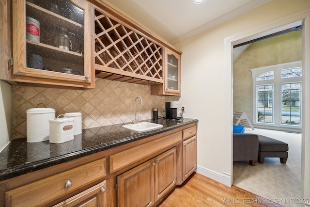 bar with sink, crown molding, light hardwood / wood-style flooring, dark stone countertops, and backsplash