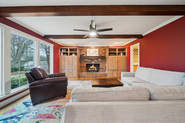 living room featuring beamed ceiling, hardwood / wood-style flooring, ornamental molding, ceiling fan, and a brick fireplace