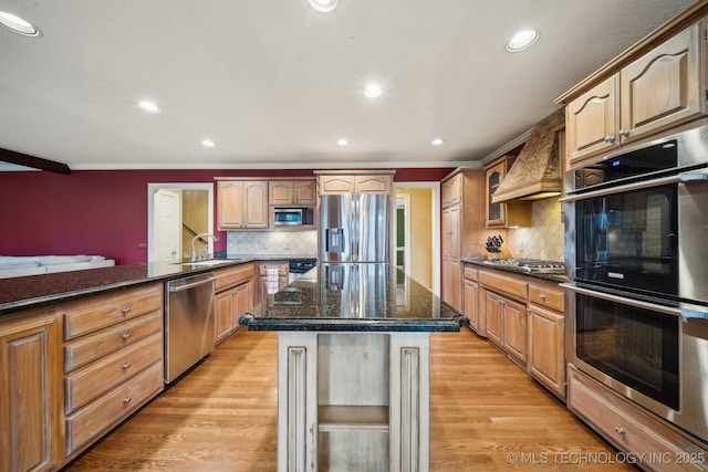 kitchen featuring premium range hood, a center island, dark stone countertops, appliances with stainless steel finishes, and light hardwood / wood-style floors