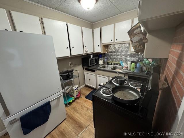 kitchen with sink, white cabinetry, light hardwood / wood-style flooring, white fridge, and backsplash