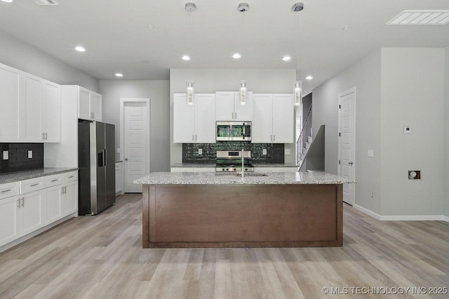 kitchen featuring decorative light fixtures, a center island with sink, appliances with stainless steel finishes, light stone countertops, and white cabinets