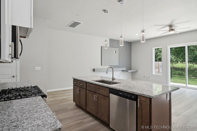 kitchen with sink, light stone counters, decorative light fixtures, dark brown cabinets, and stainless steel dishwasher